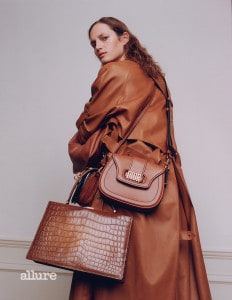 Feature, accessories, classic, heirloom, neutral palette, model, curly hair, natural look, turning, shows back, wears leather trench coat, selection of brown bags